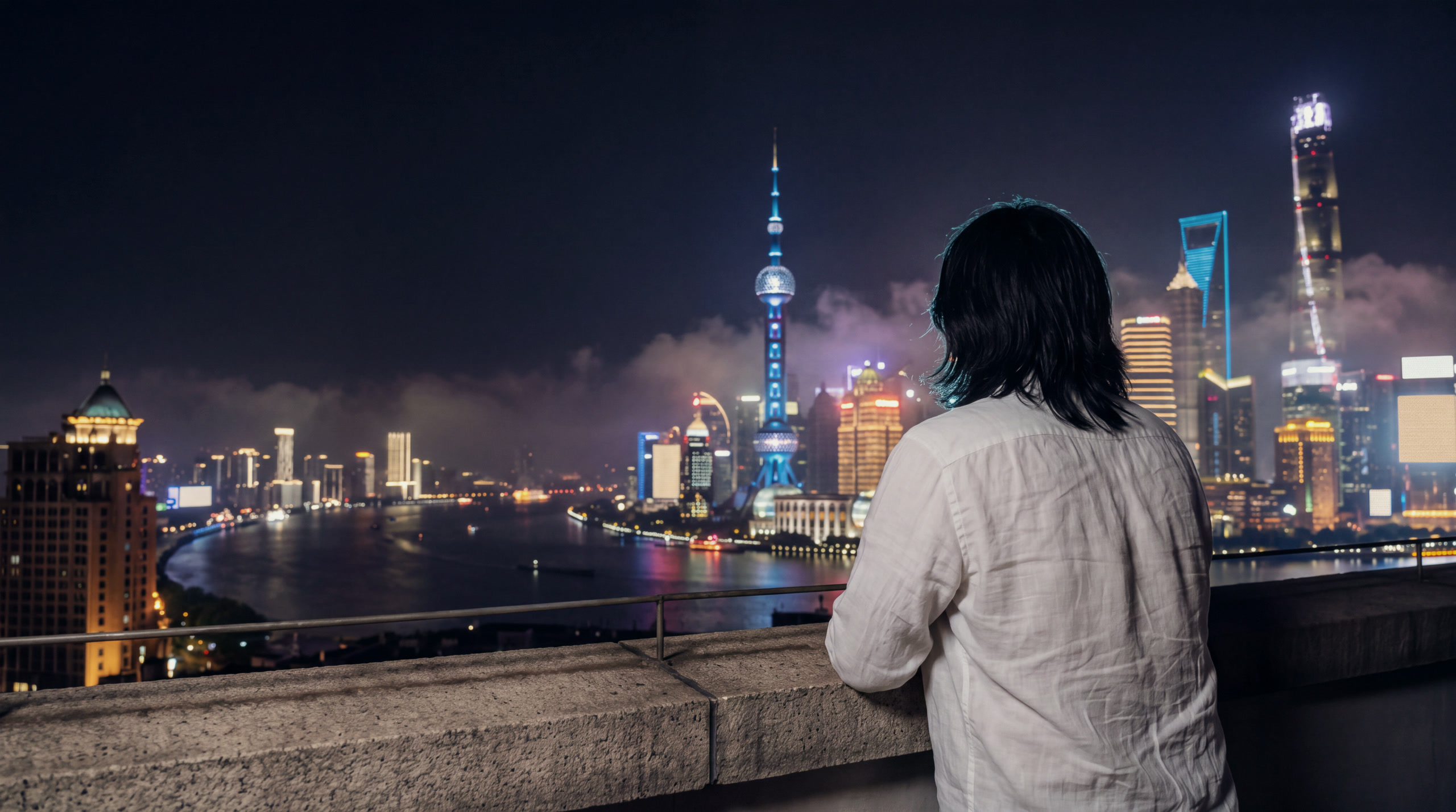 Fotografia noturna: uma pessoa de costas, de camisa branca, apoiada no parapeito de um terraço, olhando o skyline iluminado de Xangai com névoa baixa.